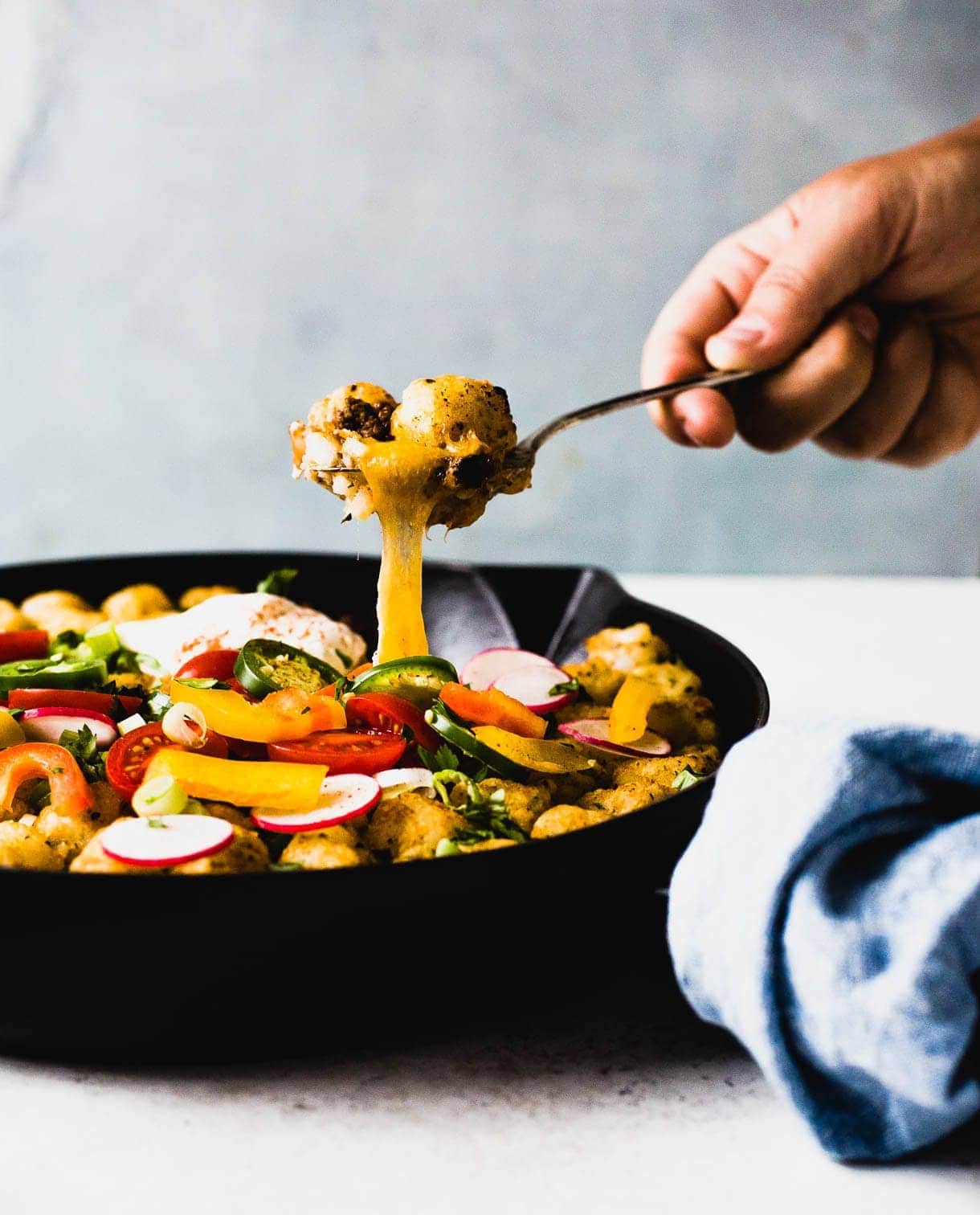 person scooping tater tot hotdish out of pan, side angle, cheese pull