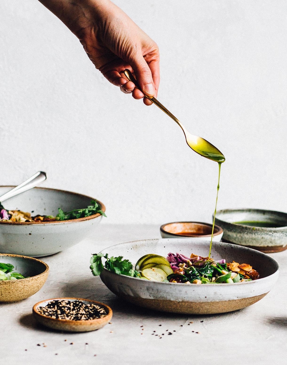 Drizzling cilantro oil on congee rice bowls, with sesame seeds in foreground.