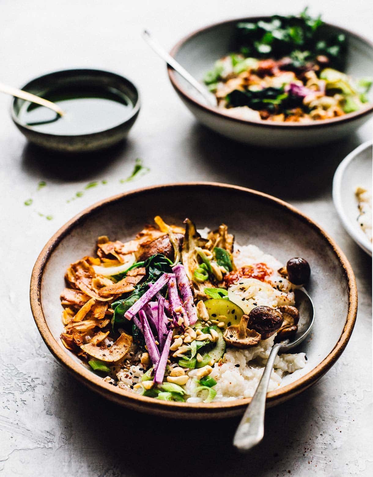 bowls of vegetarian congee with lots of fresh vegetables with black and white sesame seeds in foreground
