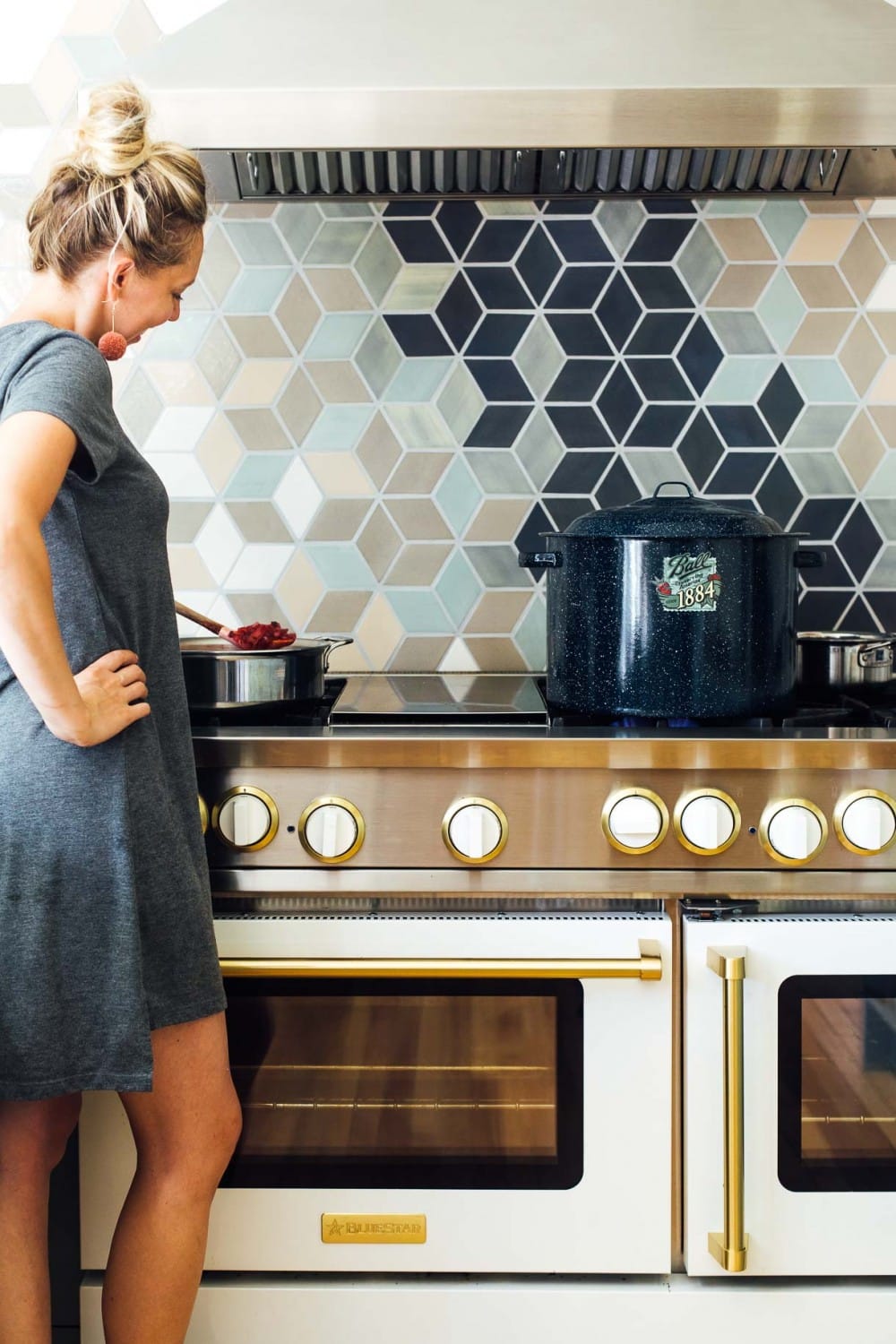 girl standing at stove with ball water bath canner on stove and she is stirring something in a saucepan