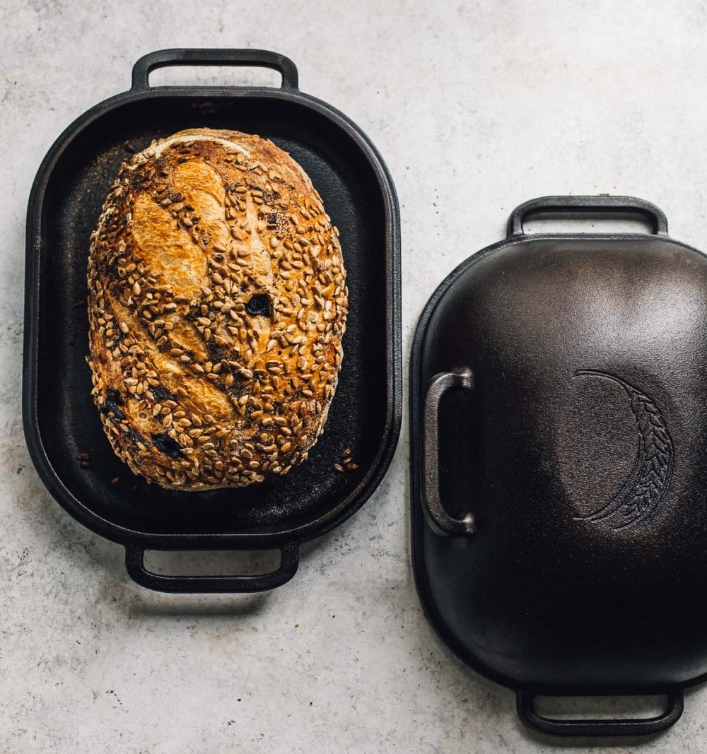 seeded sourdough bread showing resting in a cast iron baking pan