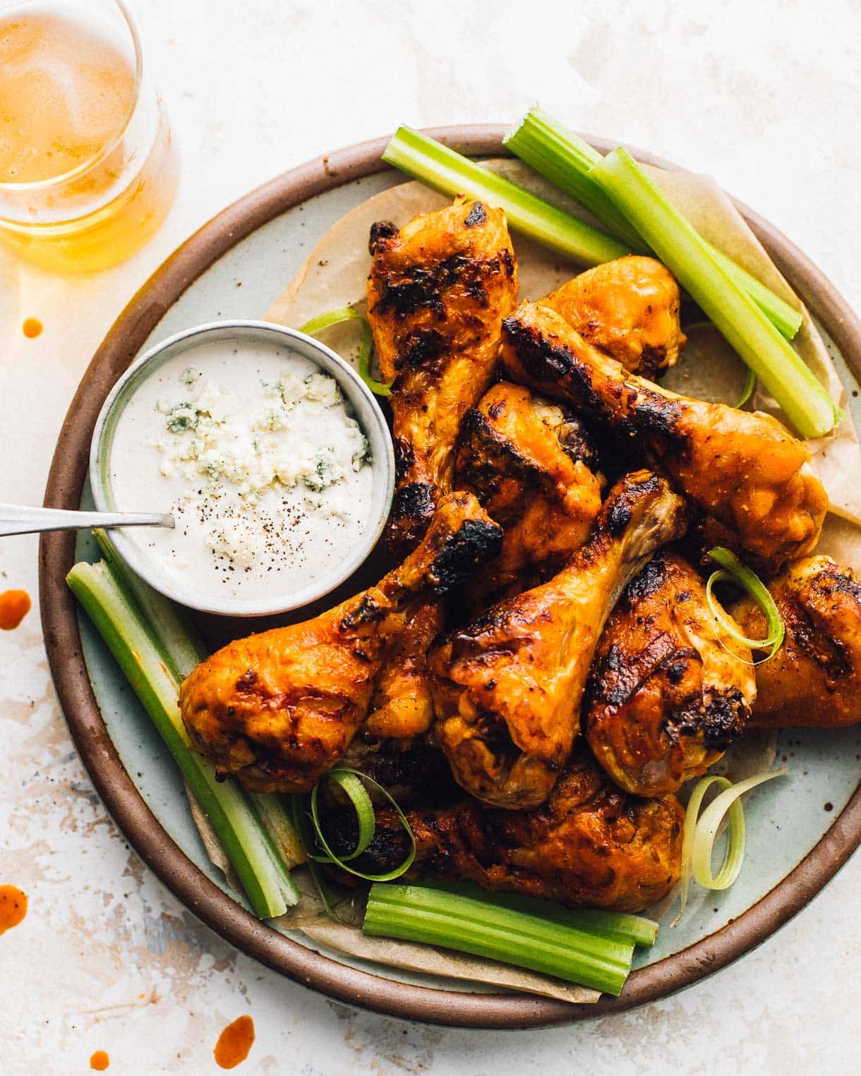 buffalo grilled chicken drummies on a plate, with a blue cheese dressing in small bowl next to it. glass of beer in upper left of photo.