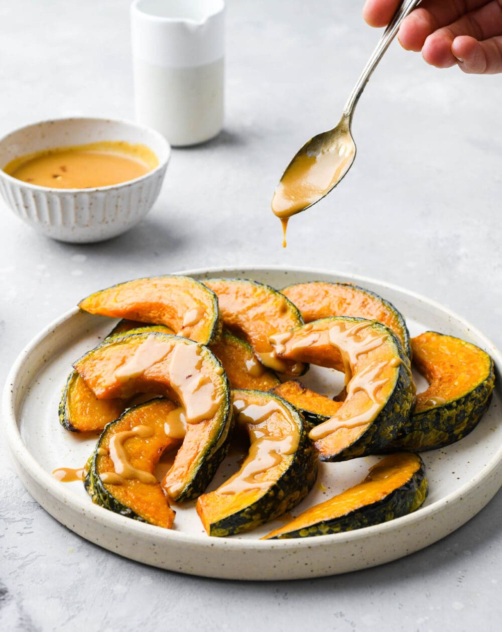 drizzling miso glaze on kabocha squash that it on a white plate.