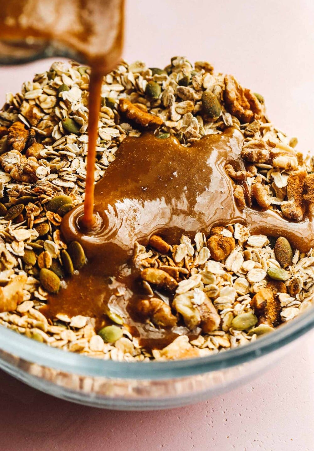 pouring wet batter over sourdough granola in a glass bowl