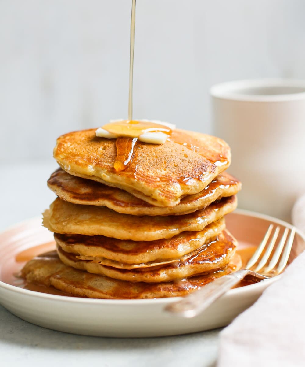 pouring maple syrup over stack of sourdough pancakes