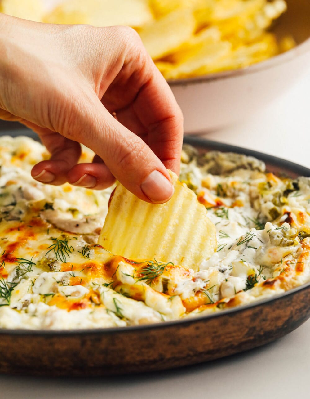 cheesy baked pickle dip with someone taking a scoop out of it with potato chip