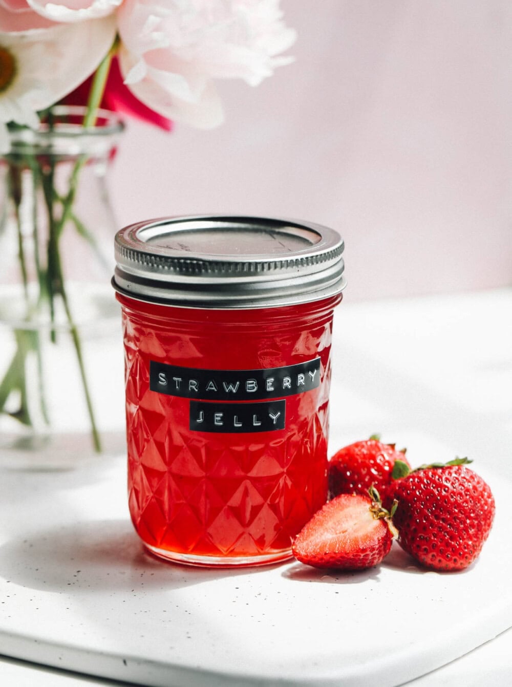 strawberry jelly in a jar with a label and flowers behind it