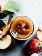 homemade apple butter in a glass jar with apples surrounding